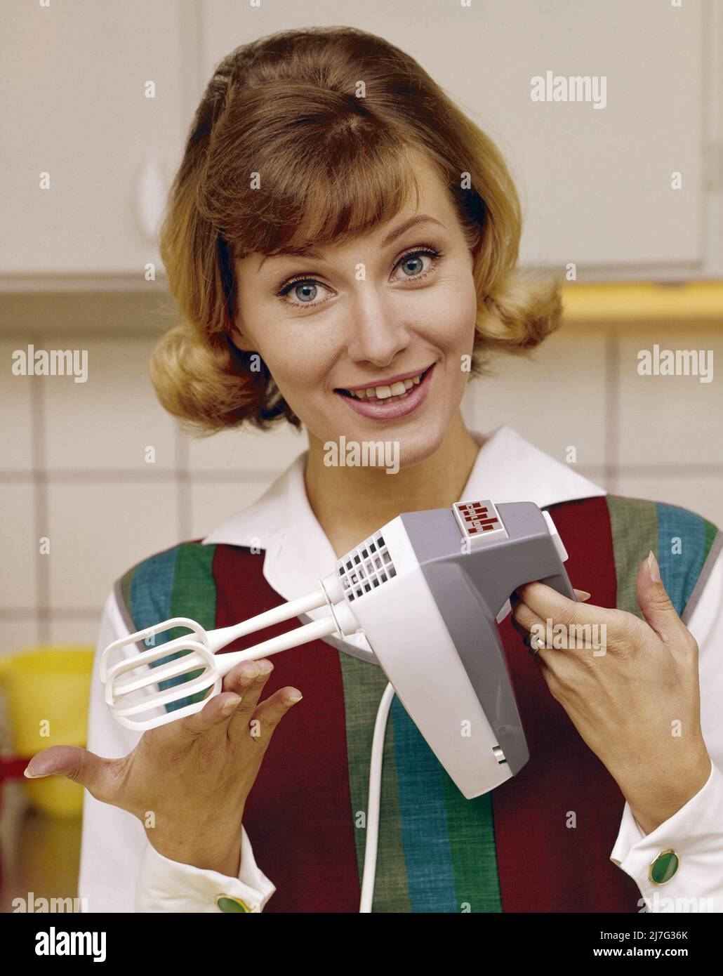 In the 1960s. A young woman pictured in the kitchen using an electric hand mixer. Stock Photo