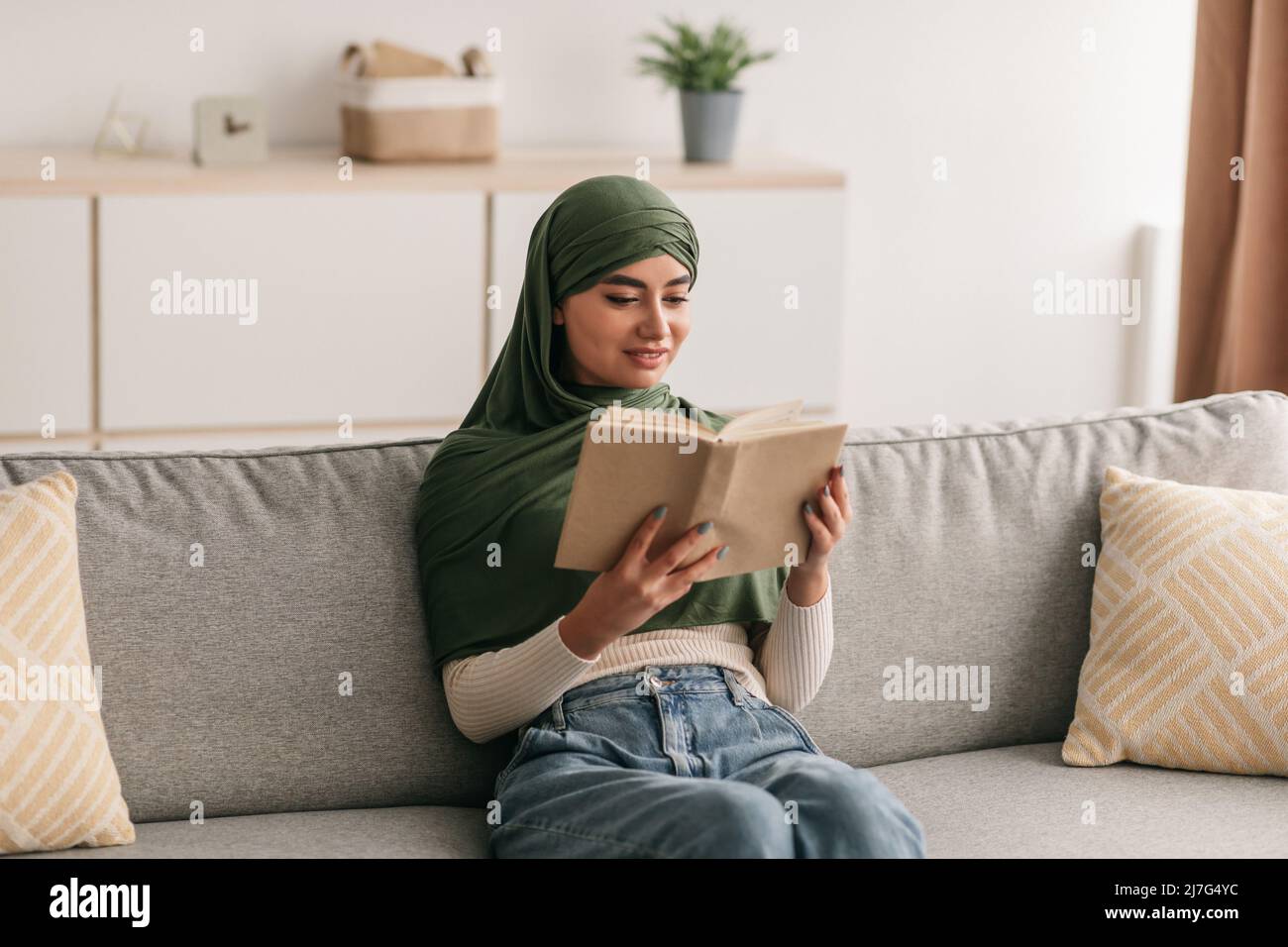 Stay home hobbies. Beautiful young Arab woman in hijab reading book ...