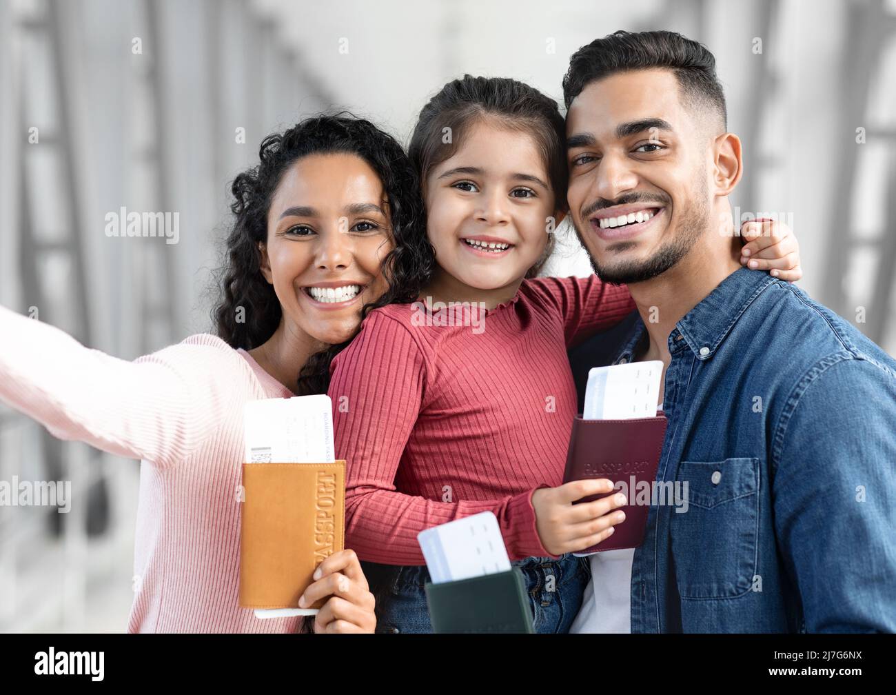 Joyful Young Arabic Parents And Little Daughter Taking Selfie At Airport Stock Photo