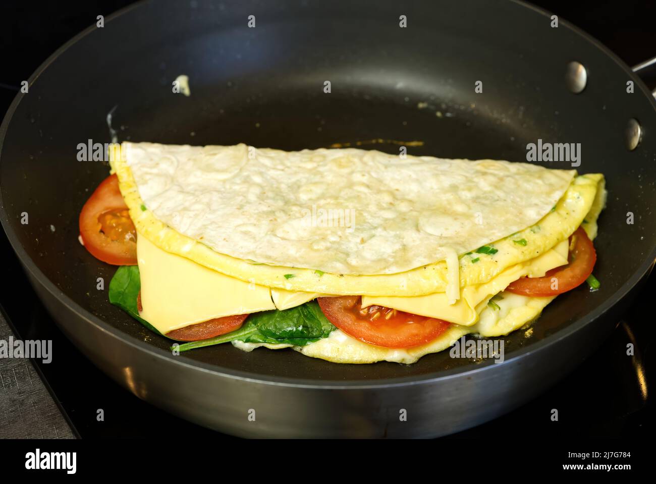 Pita wrap with tomatoes, cheese, ham and spinach on the frying pan