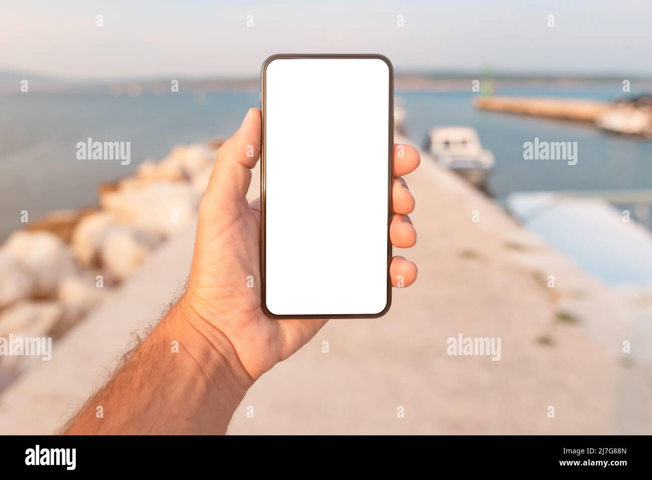 Man standing by the sea and holding mobile smart phone with blank mockup screen, closeup of hand and device, selective focus Stock Photo