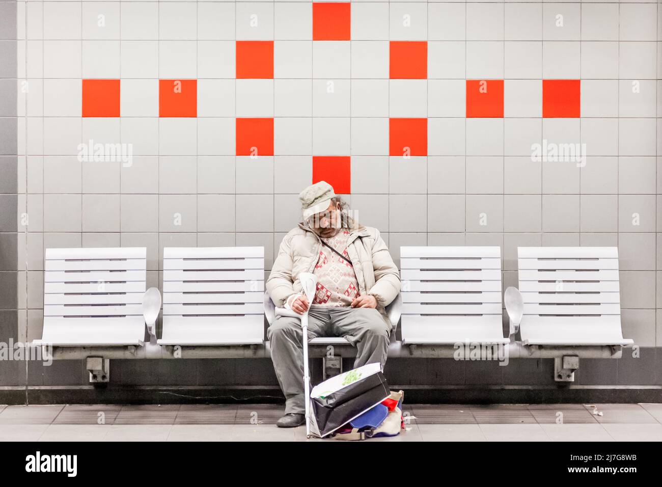 Old man dozing on a bench in a subway station. White wall and red tiles. Brussels. Stock Photo