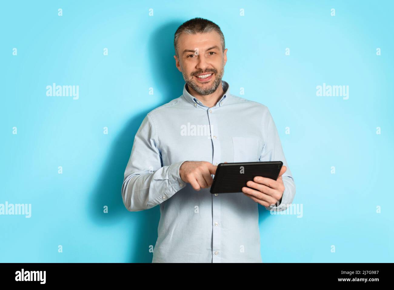 Middle Aged Man Using Tablet Browsing Internet On Blue Background Stock Photo