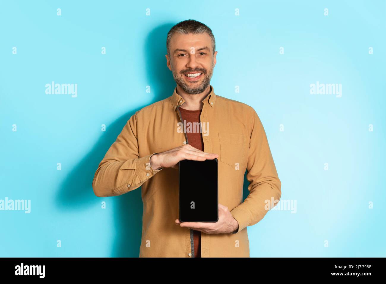 Male Holding Tablet Computer With Empty Screen On Blue Background Stock Photo