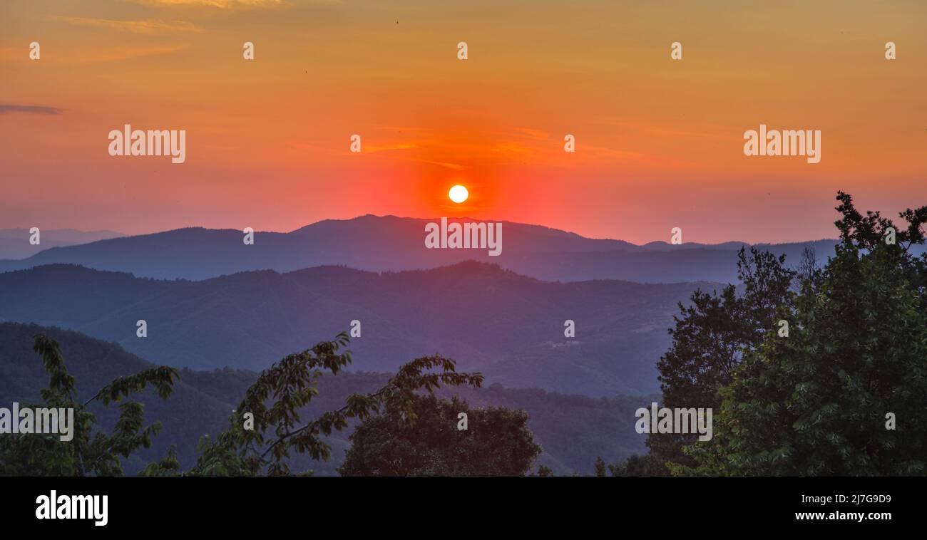 Intense and orange colored sky during sunset in tuscany. Mountain silhouettes in the distance. Amazing view of the spectacular countryside. Italy. Stock Photo