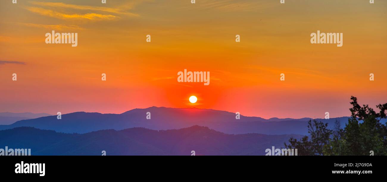 Intense and orange colored sky during sunset in tuscany. Mountain silhouettes in the distance. Amazing view of the spectacular countryside. Italy. Stock Photo