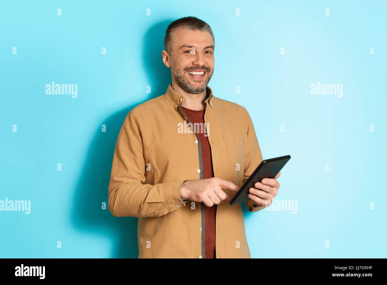 Middle Aged Business Man Using Digital Tablet Over Blue Background Stock Photo