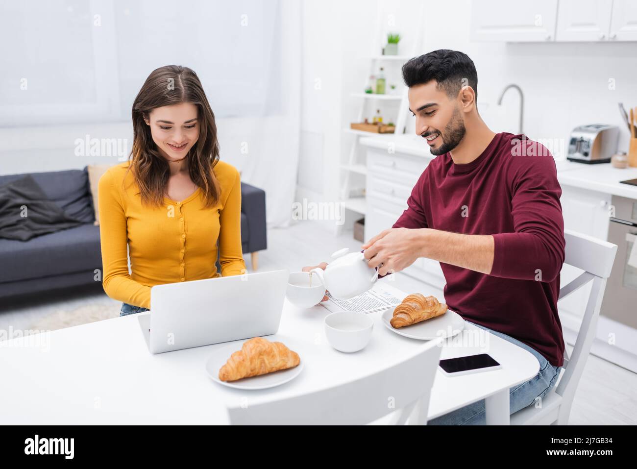 Cheerful interracial couple using laptop near breakfast in kitchen Stock Photo