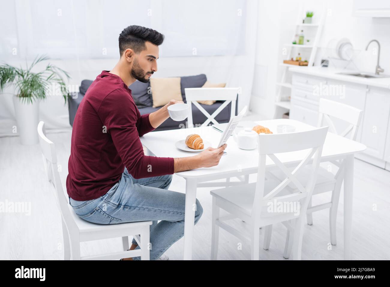 Side view of arabian man reading news and holding cup near breakfast in kitchen Stock Photo