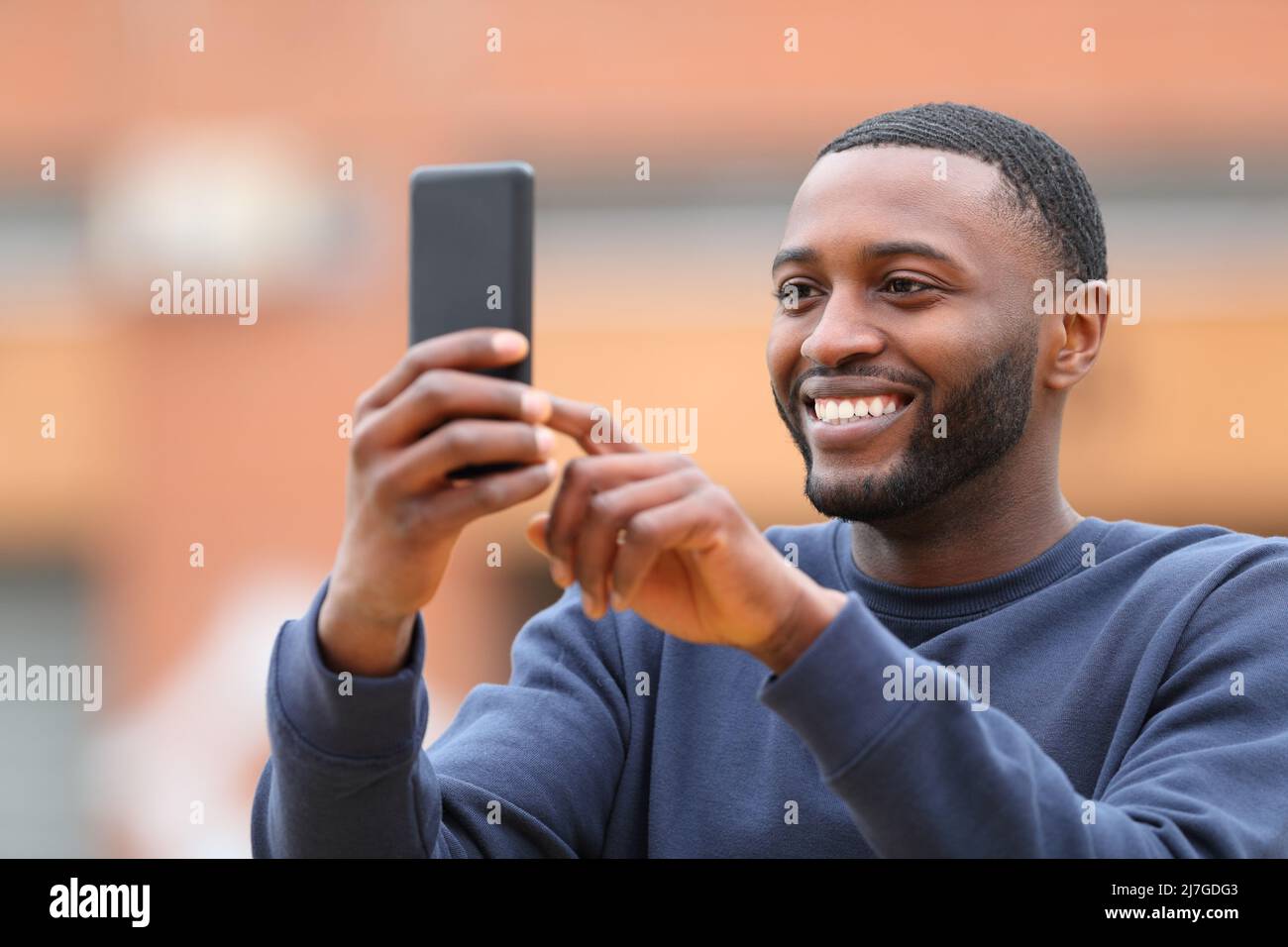 Happy man with black skin taking selfie or photo with smart phone standing in the street Stock Photo