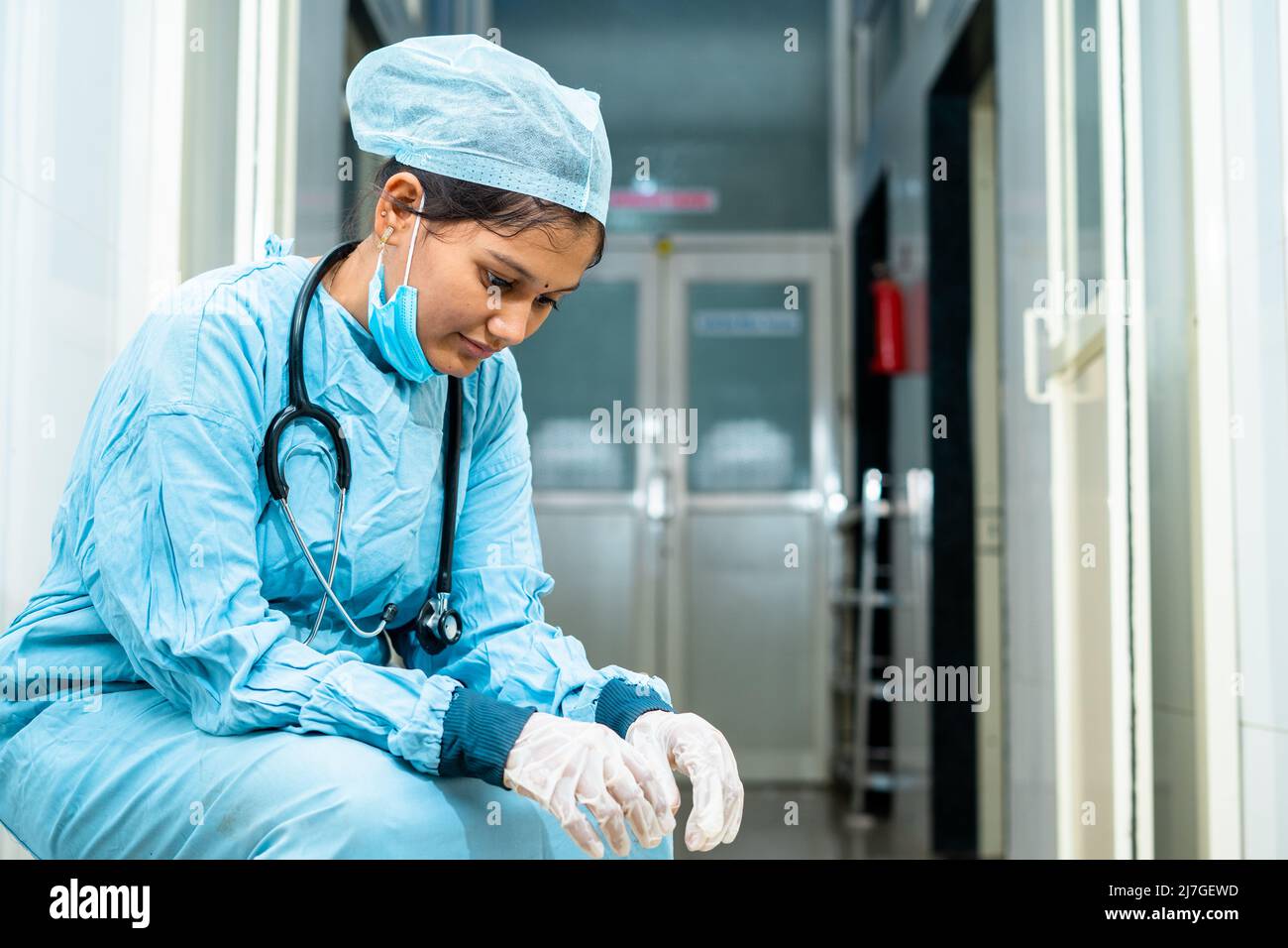 thoughtful medical practitioner in operation gown sitting outside the operation theatre - concept of overwork, exhausted and job loss Stock Photo