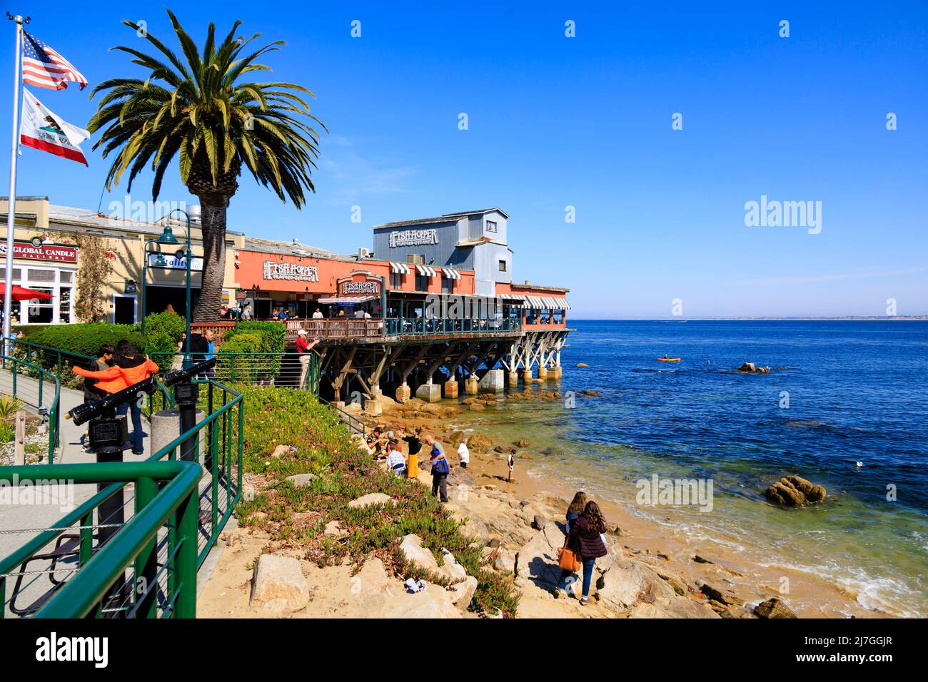 The Fish Hopper seafood and steak restaurant juts out into the Pacific Ocean on a pier. Tourists on the beach .Cannery Row, Monterey, California, USA. Stock Photo
