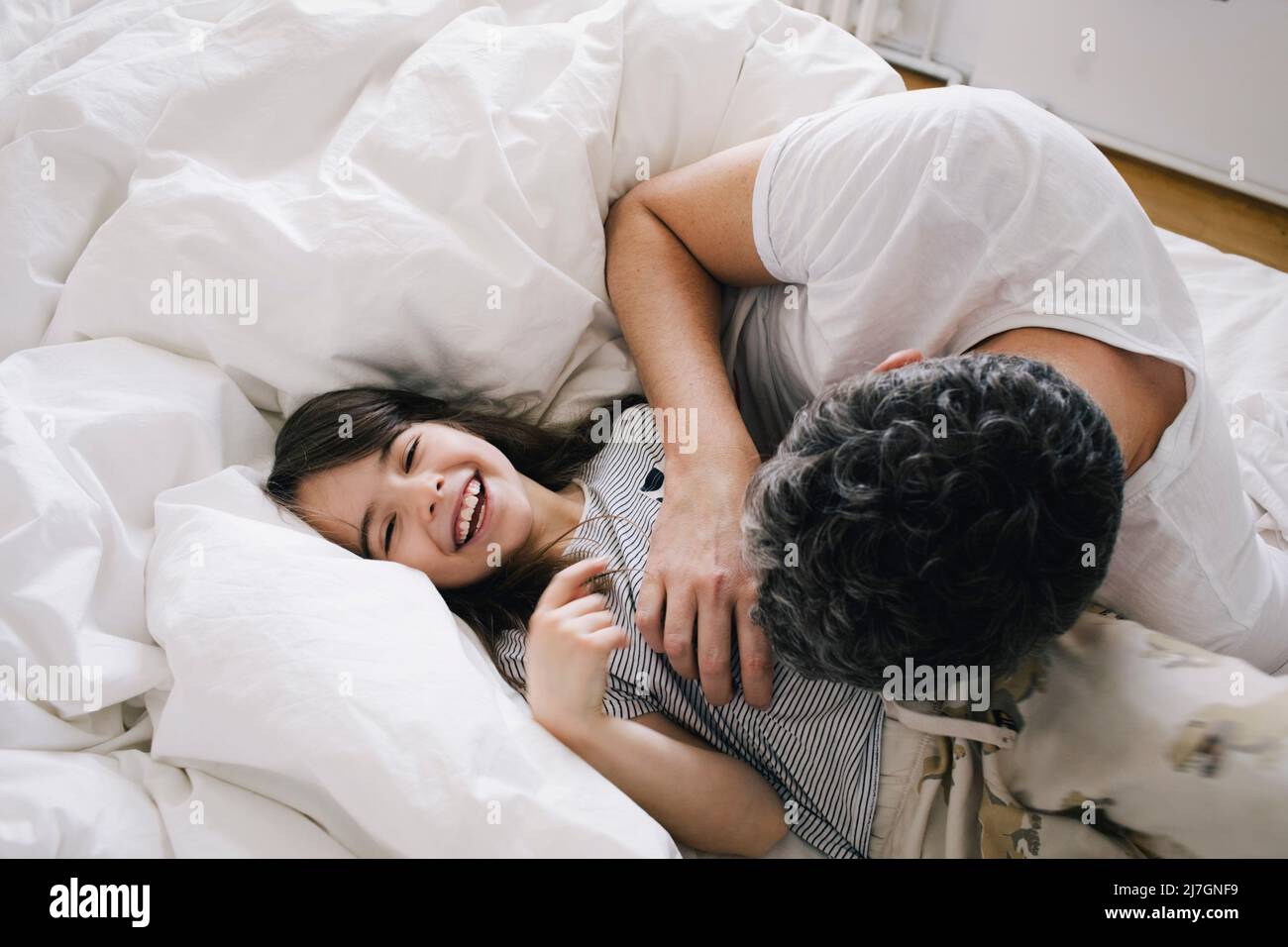Playful father playing with daughter lying on bed at home Stock Photo