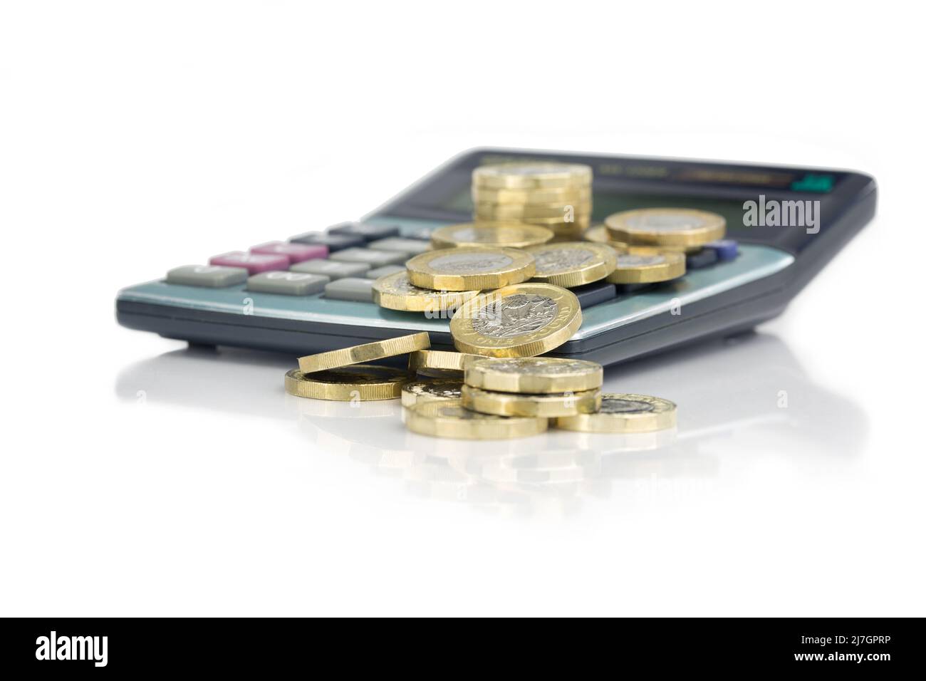 Calculator with UK Pound Sterling GBP gold coloured coins falling over to the front on a white reflective background Stock Photo