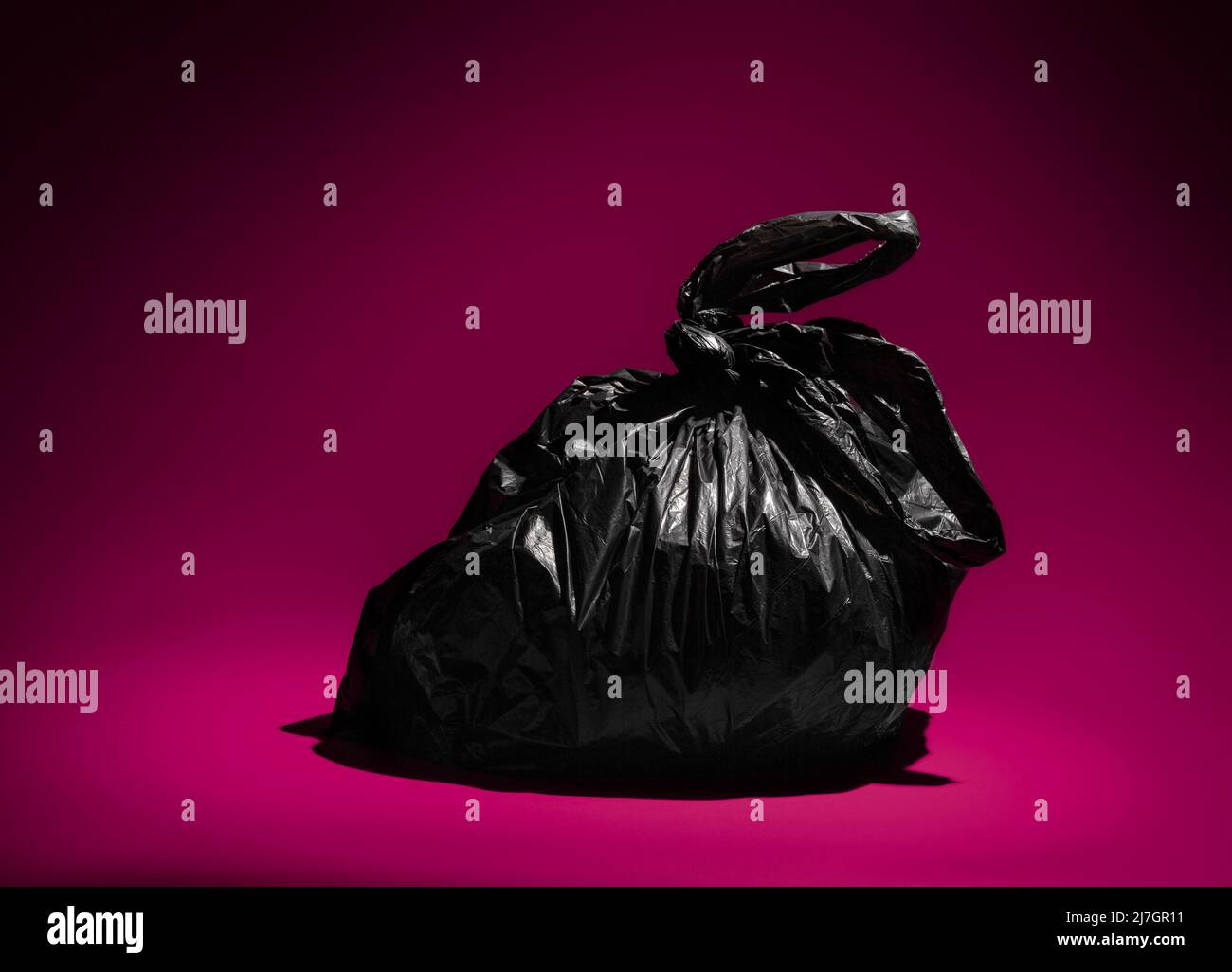 Black plastic trash bin bag on a purple background Stock Photo