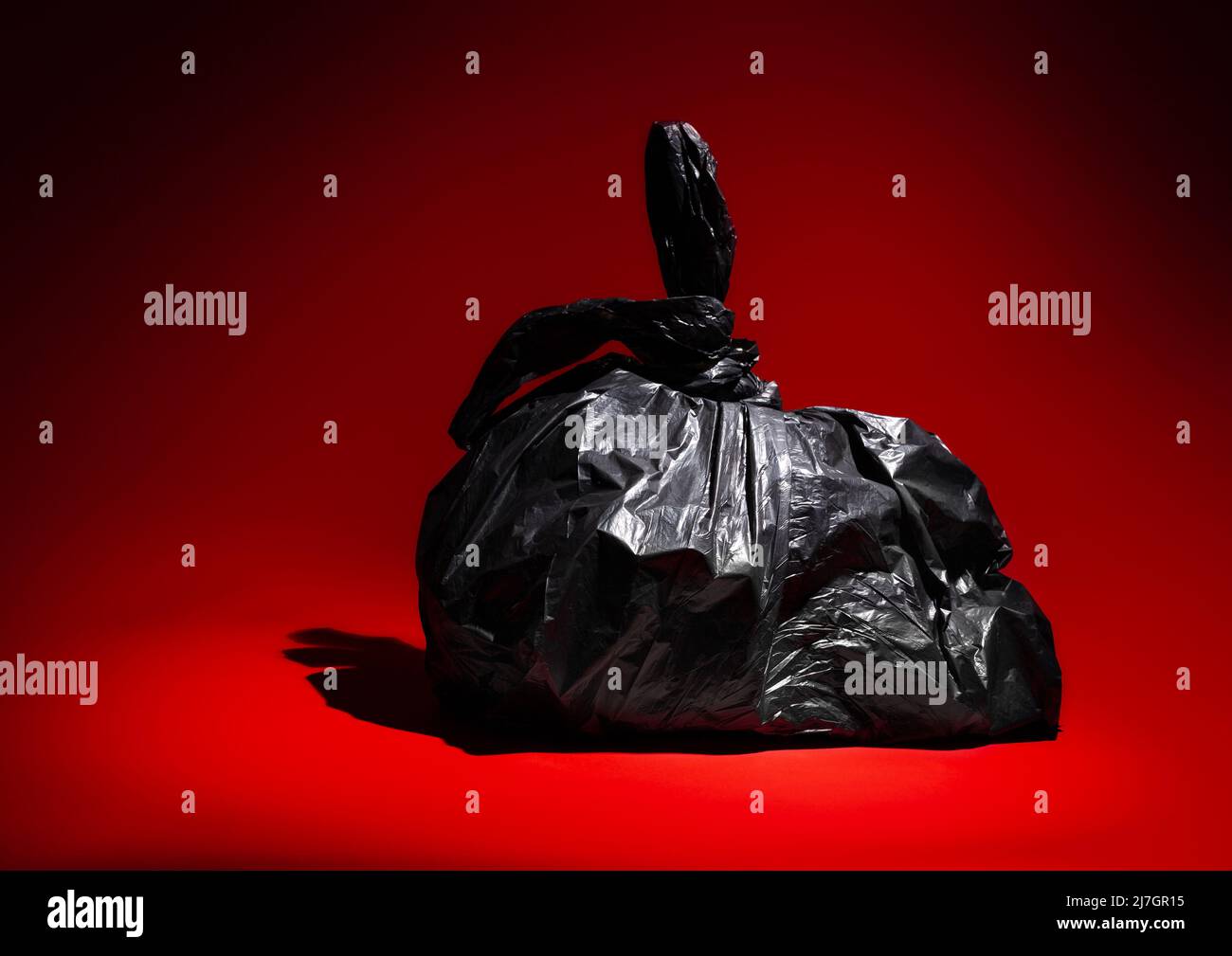 Black Plastic Trash Bin Bag on a Red Background Stock Photo
