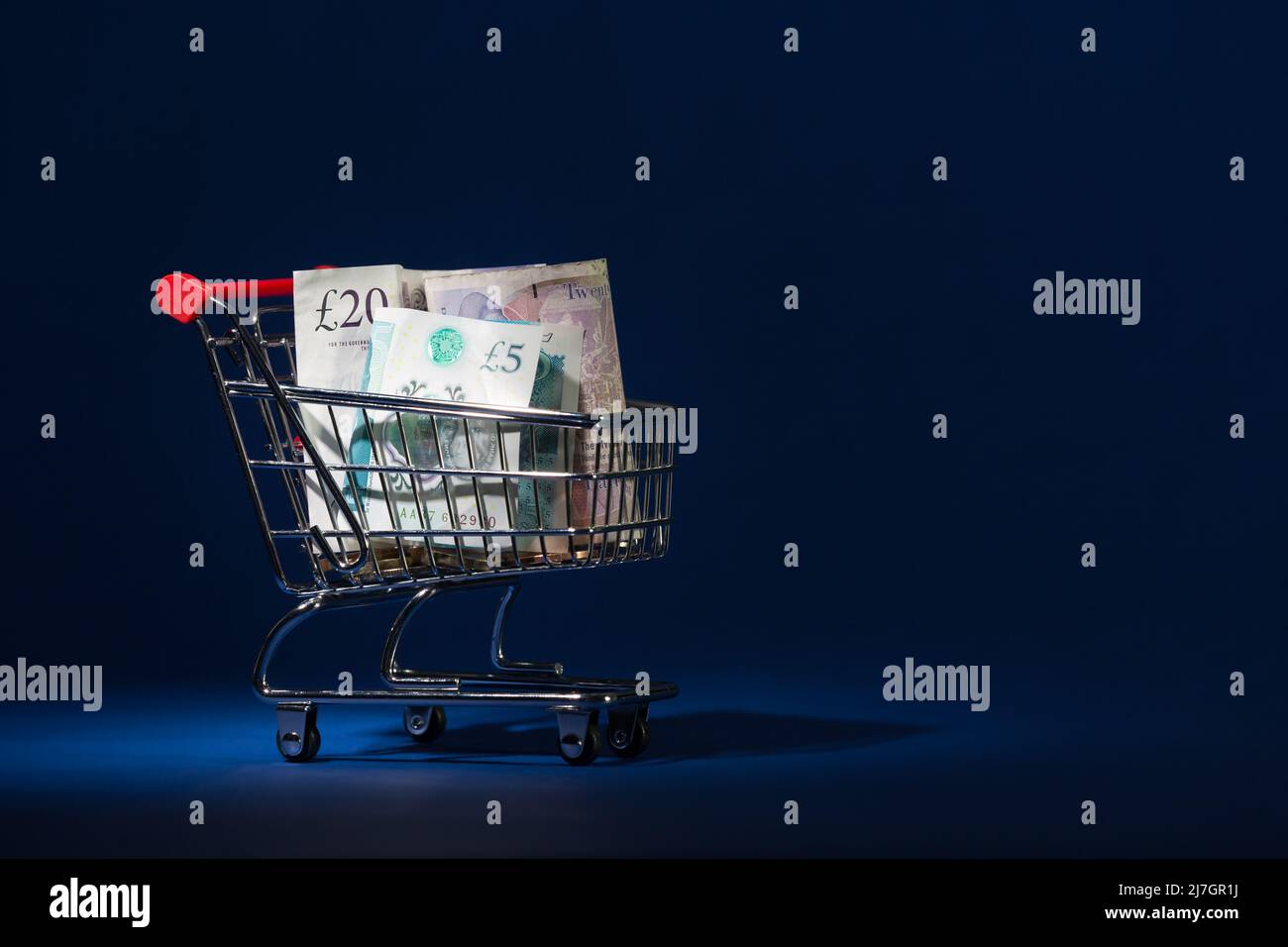 Mini Shopping Cart Trolly Close Up with UK GBP Notes Pounds Sterling This store basket is on a blue background Stock Photo