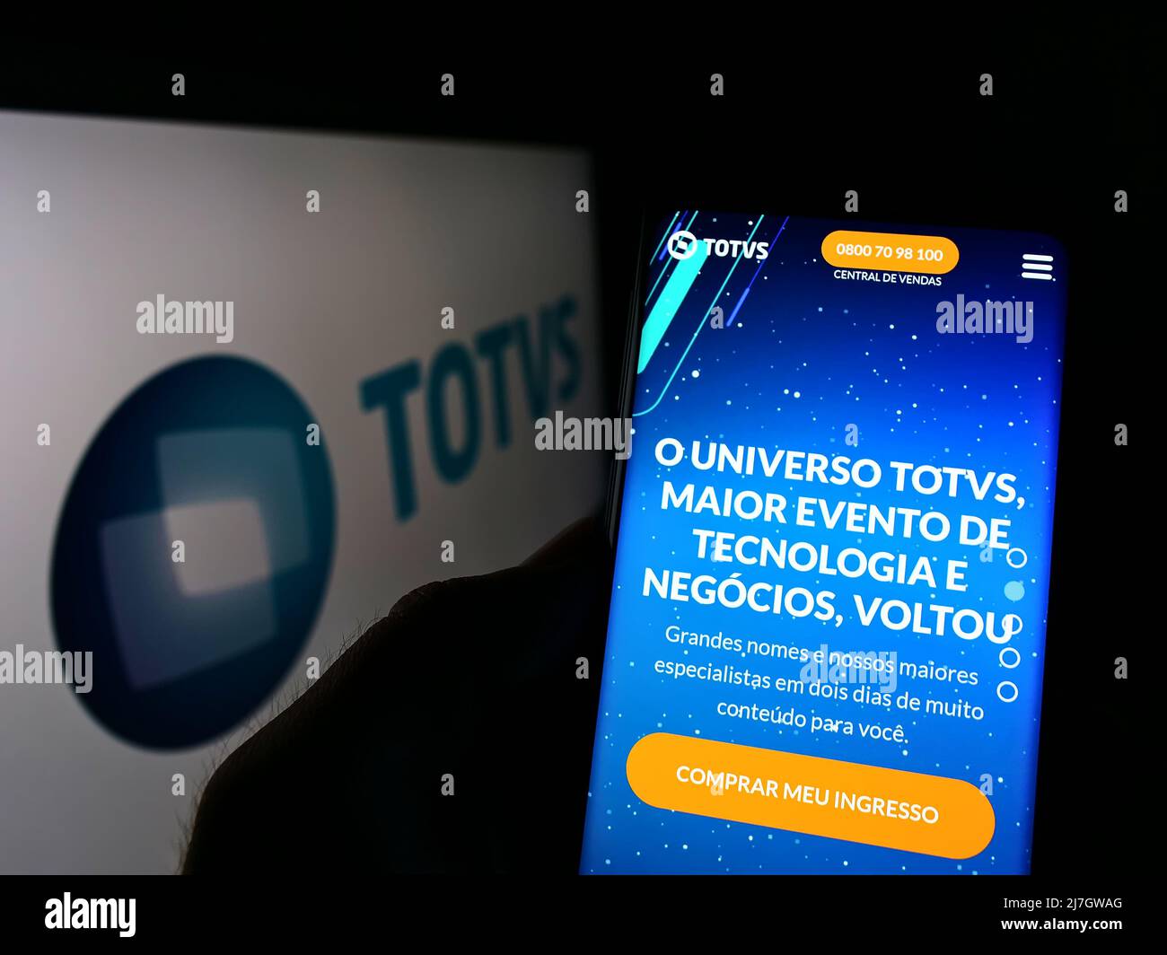 Person holding cellphone with website of Brazilian software company TOTVS SA on screen in front of logo. Focus on center of phone display. Stock Photo