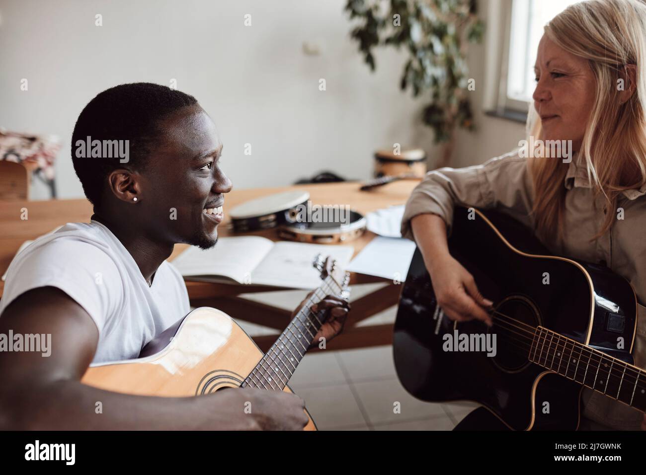 Smiling female mature tutor teaching guitar to young man in classroom Stock Photo
