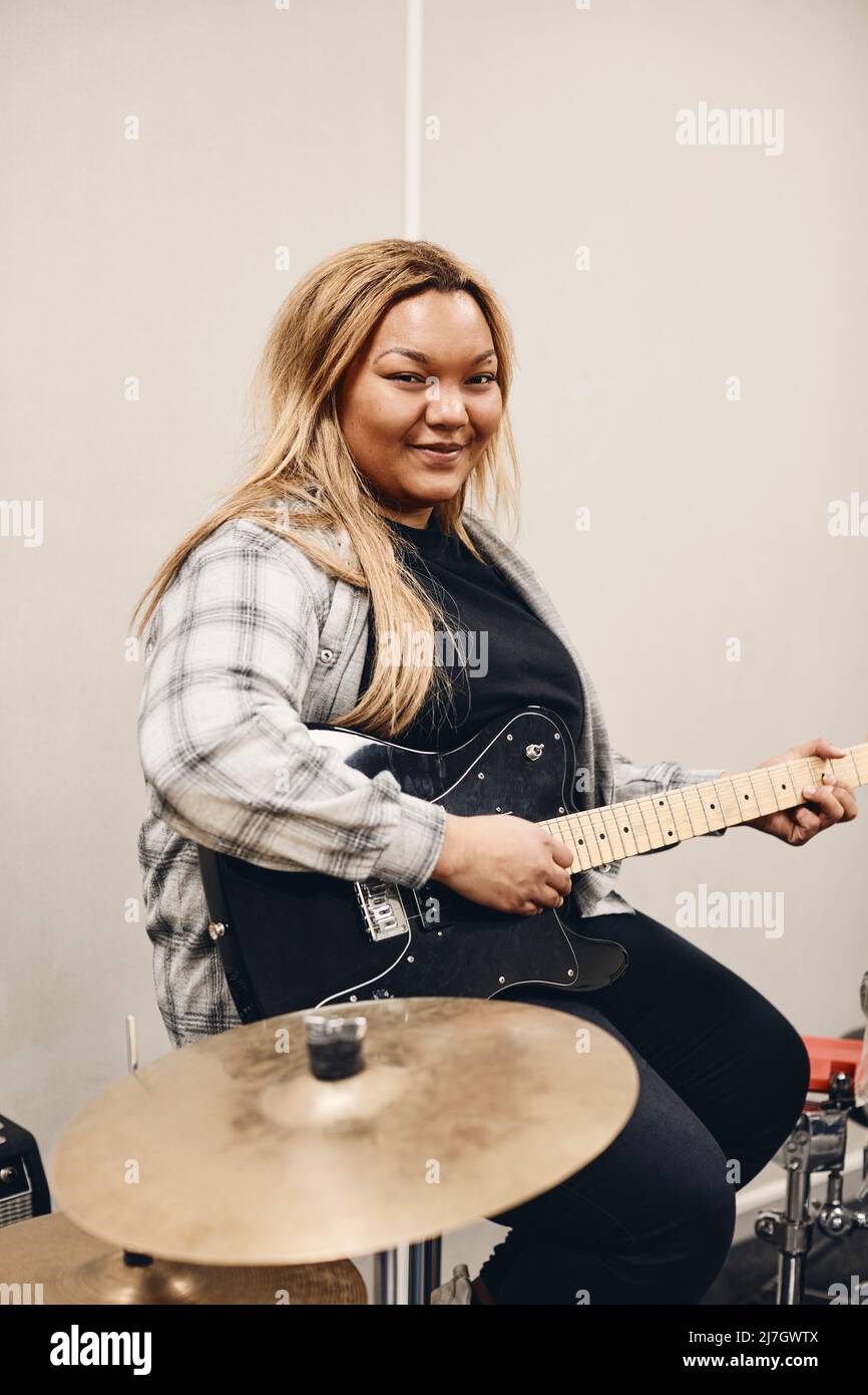 Portrait of smiling young woman practicing guitar in classroom Stock Photo