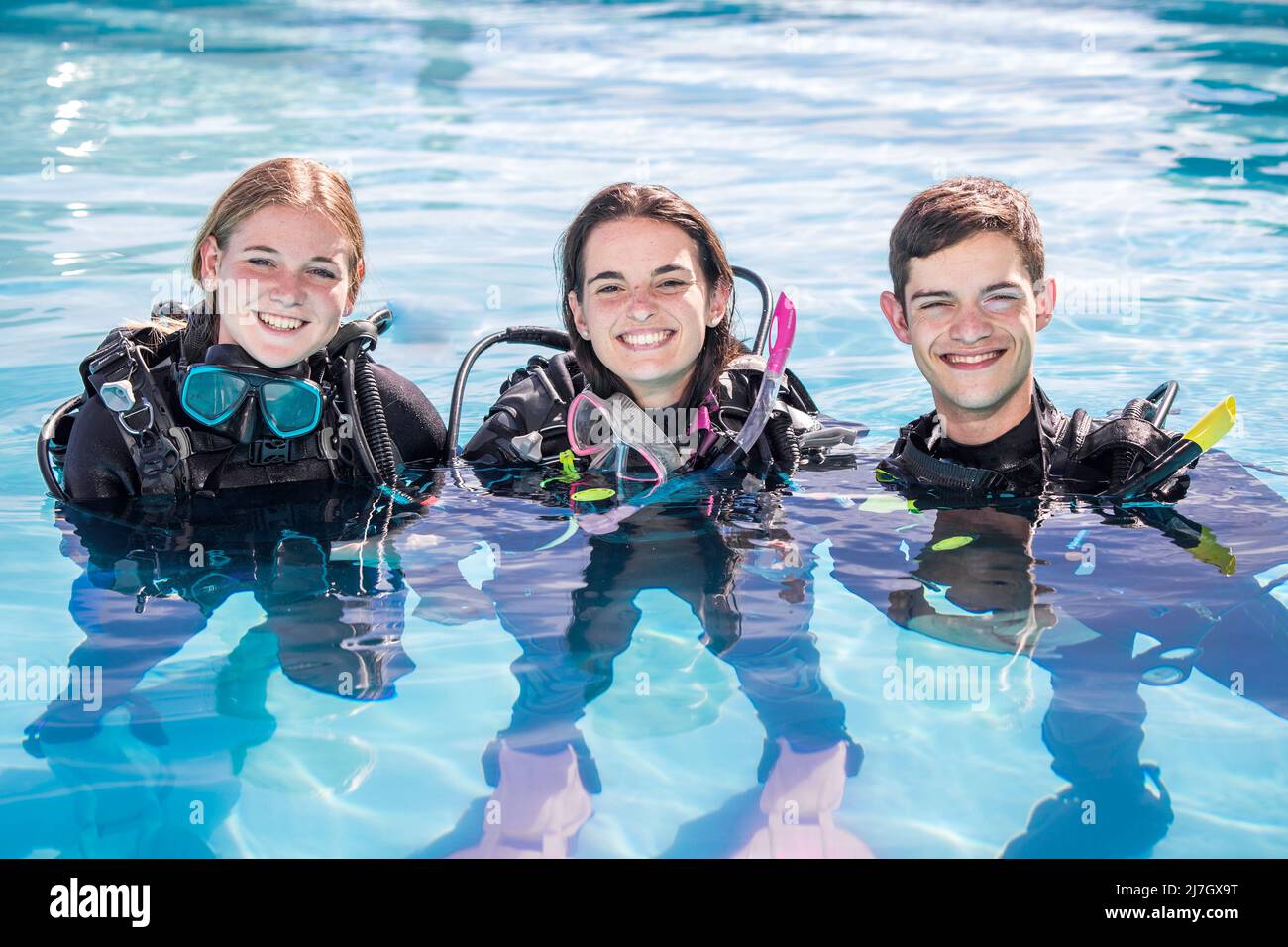 A group of happy scuba divers standing in a pool with their gear on smiling at the camera Stock Photo