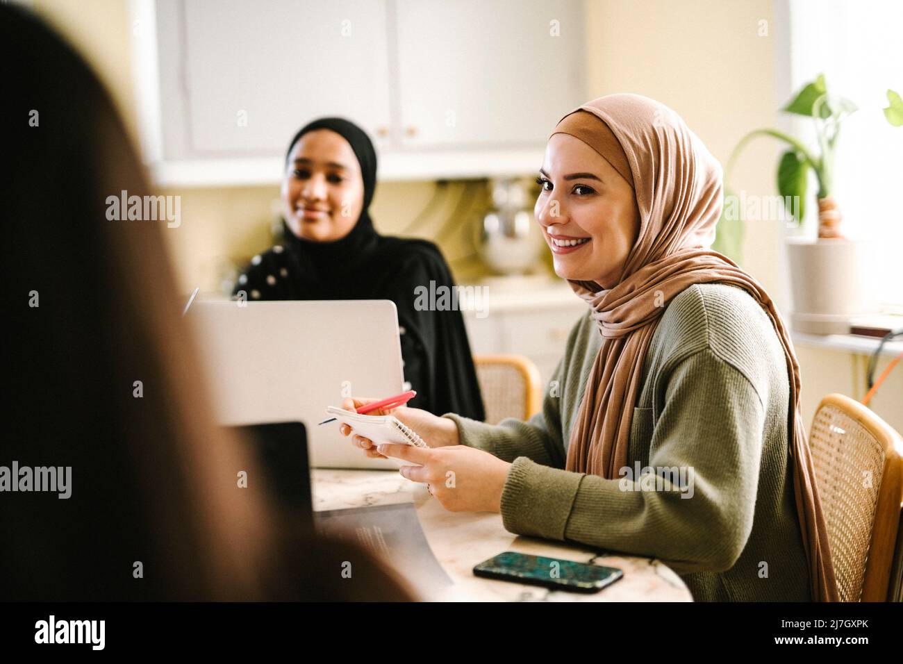 Smiling young woman in hijab studying with friends at home Stock Photo ...