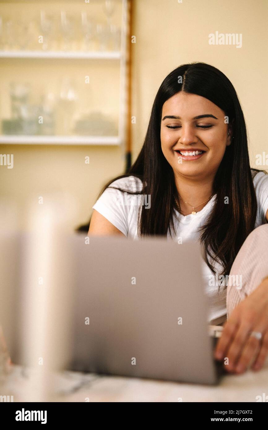 Happy young female freelancer using laptop sitting at table Stock Photo