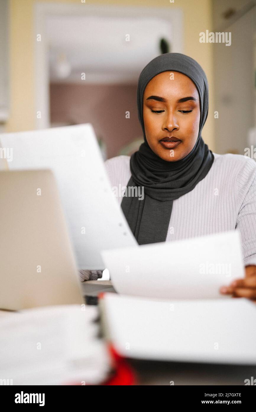 Young female freelancer analyzing documents while working from home Stock Photo