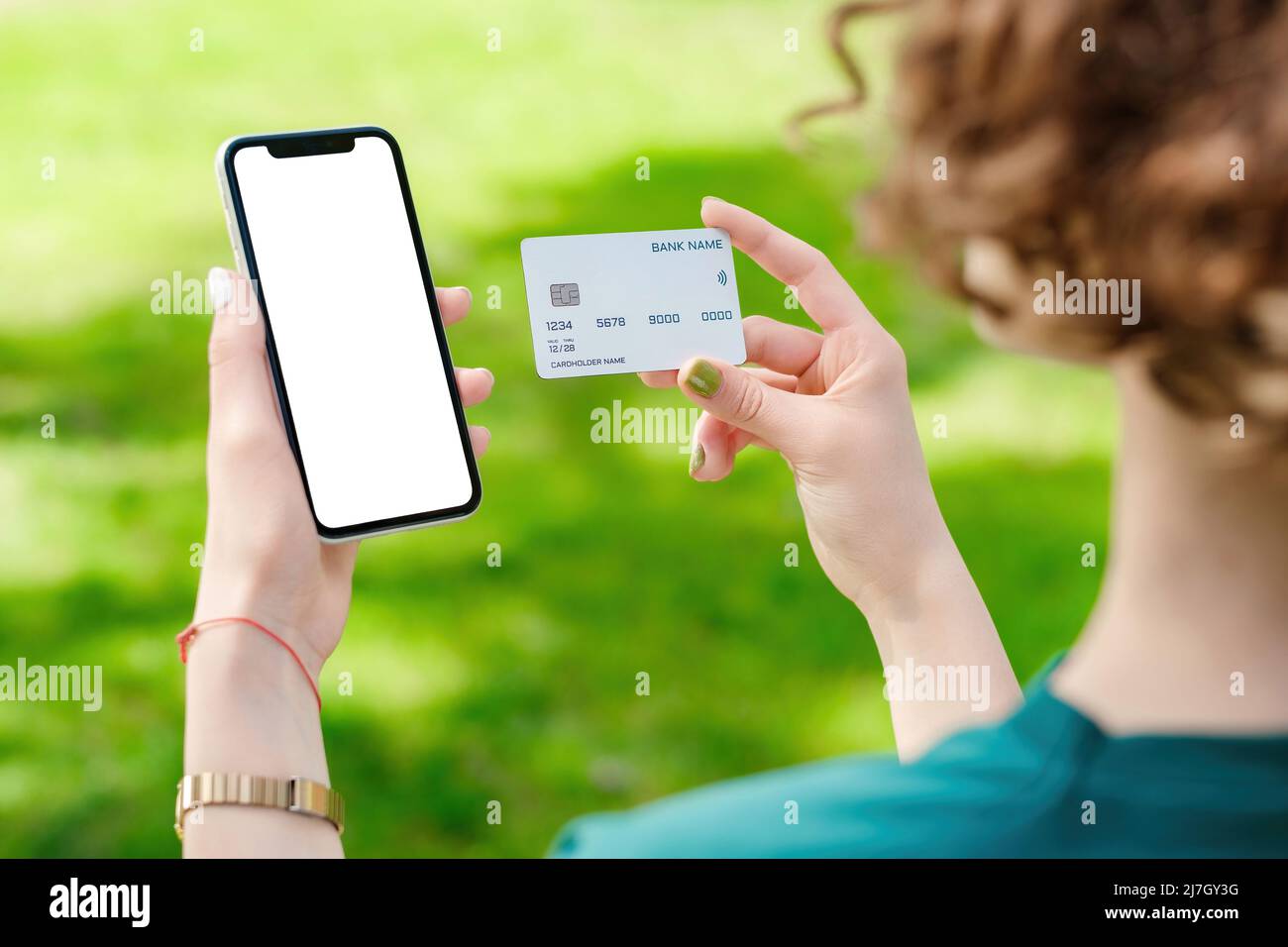 Young redhead woman or teen girl hands holding credit card and phone with mockup white blank display, empty screen for shopping or banking app. Mobile Stock Photo
