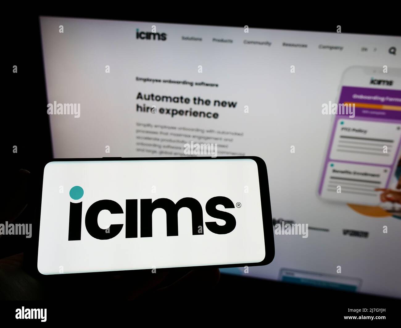 Person holding smartphone with logo of US HR software company iCIMS Inc. on screen in front of website. Focus on phone display. Stock Photo