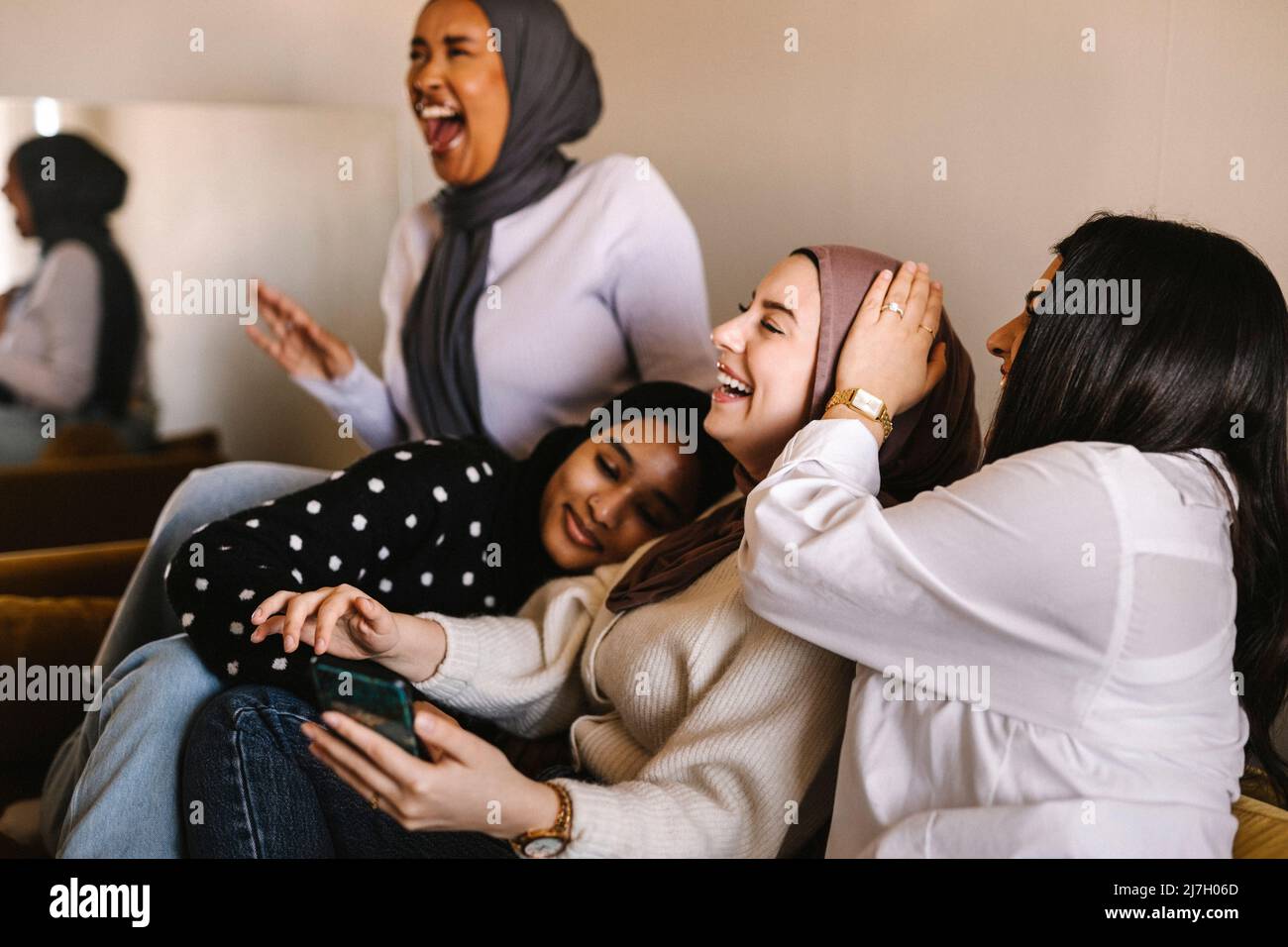 Young women laughing while sitting together on sofa at home Stock Photo