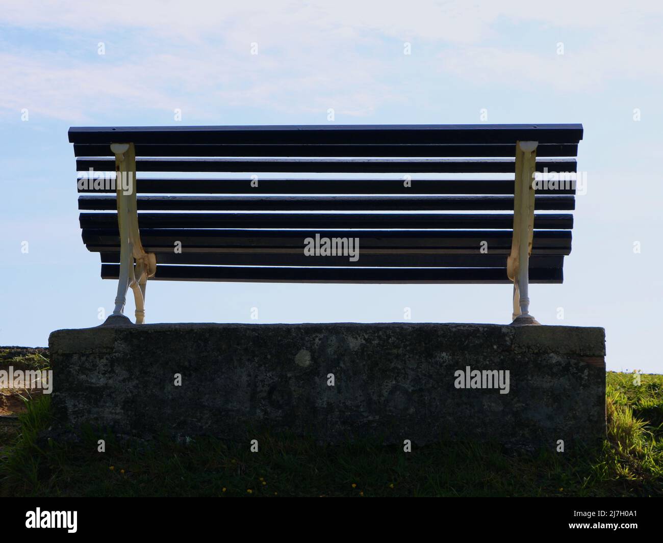 An empty park bench in morning Spring sunlight backlit on a concrete ...