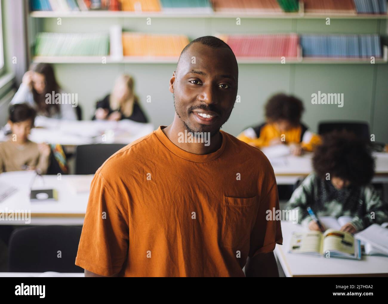 Portrait of smiling male teacher with students studying in classroom ...
