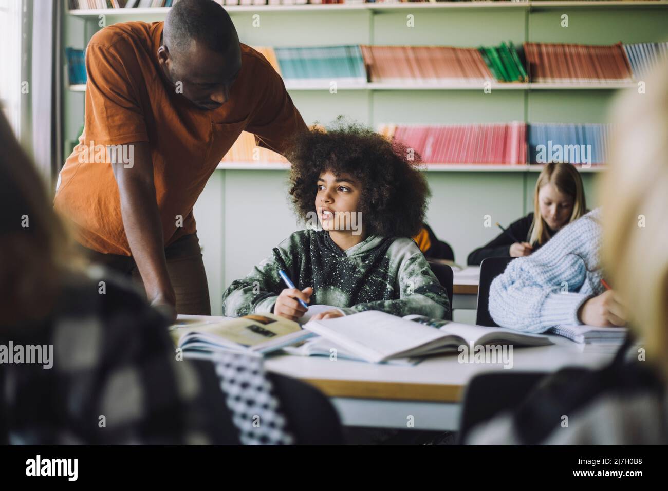 Male teacher helping student while studying in classroom Stock Photo
