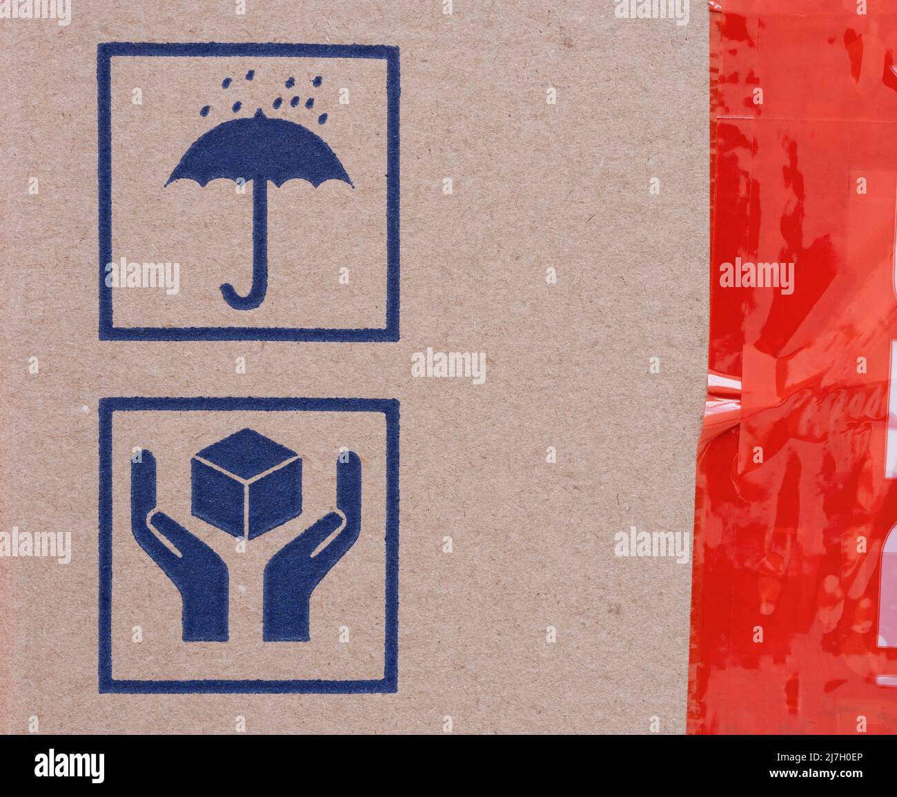 Two signs on cardboard box - Umbrella and Handle with Care, and a red scotch tape on a cardboard Stock Photo