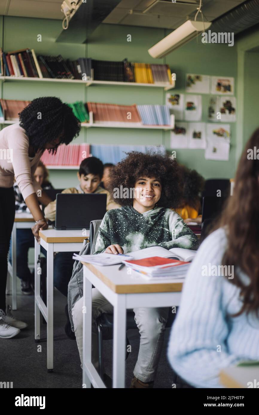 Smiling student with curly hair sitting at desk in classroom Stock Photo