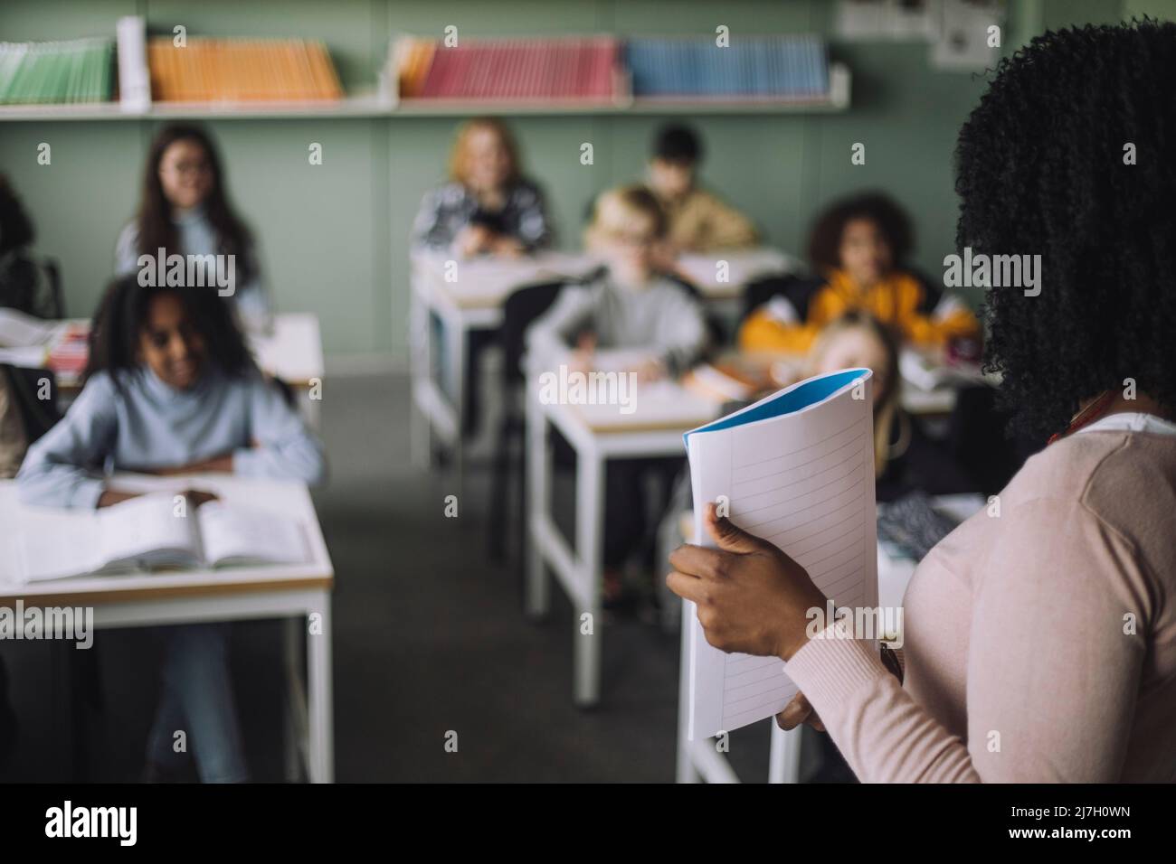 Side view of teacher showing notebook to students while teaching in classroom Stock Photo