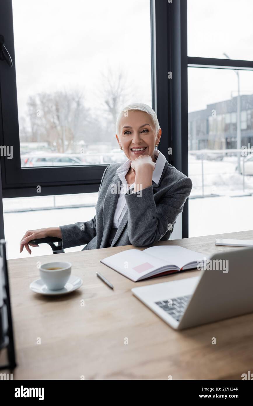 successful banker smiling at camera near blank notebook, coffee cup and ...