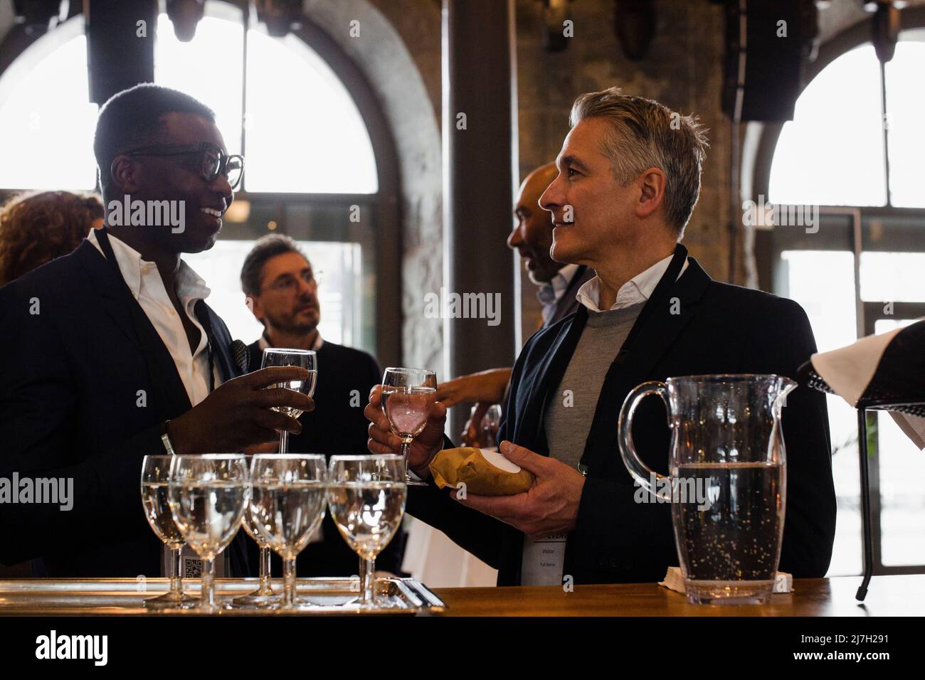 Businessmen holding glasses while discussing with each other during seminar Stock Photo