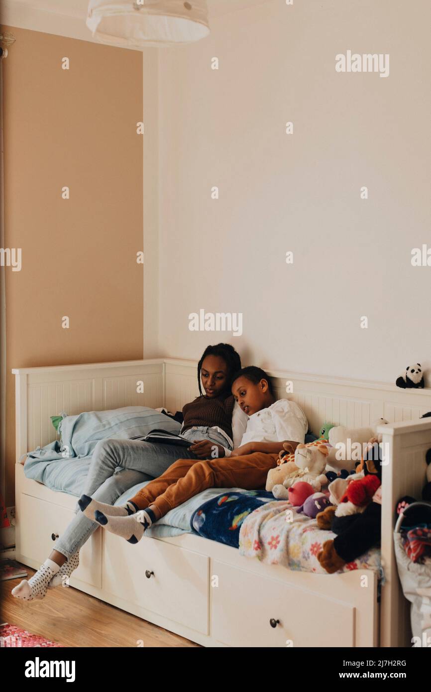 Siblings reading story book together while sitting on bed at home Stock Photo
