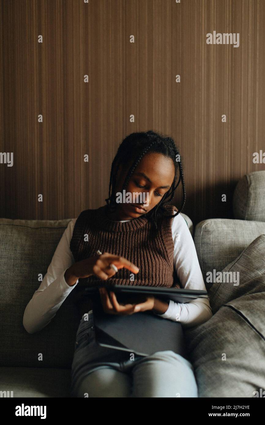 Girl using tablet PC while sitting on sofa at home Stock Photo