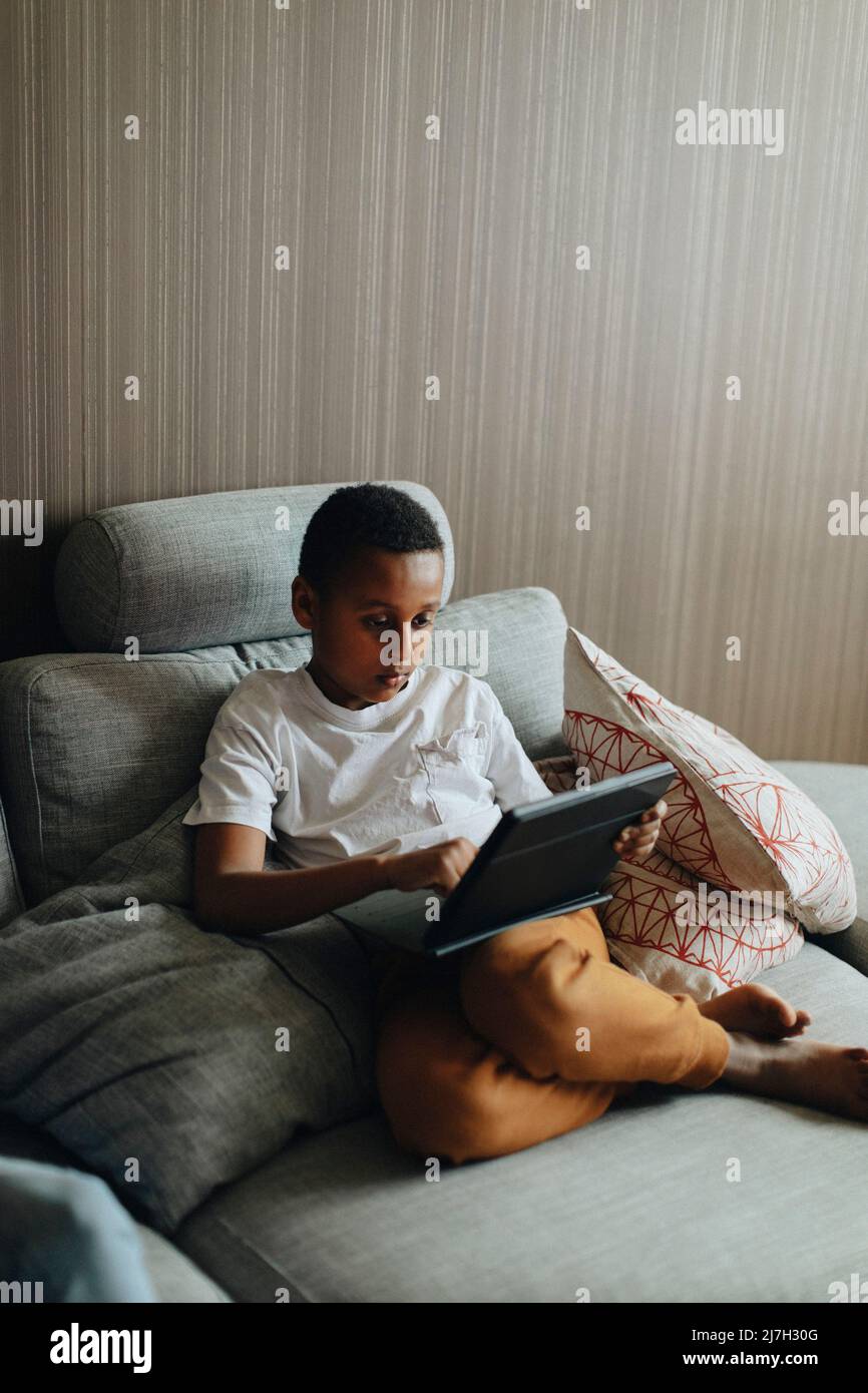 Boy using tablet PC while sitting on sofa at home Stock Photo
