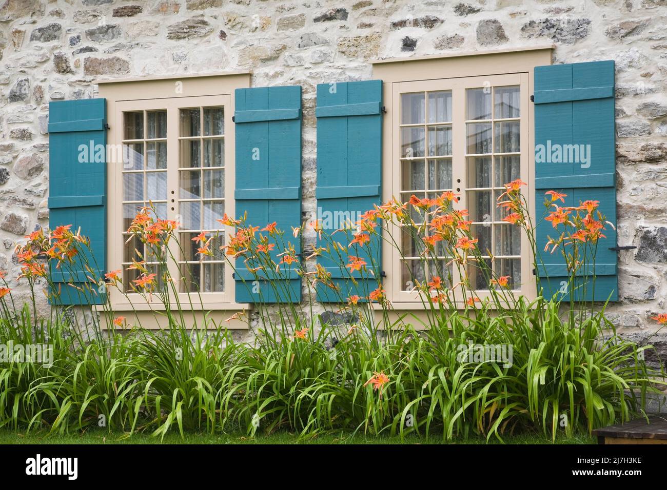 Tan wood windows with teal blue shutters on old 1722 fieldstone home in summer. Stock Photo