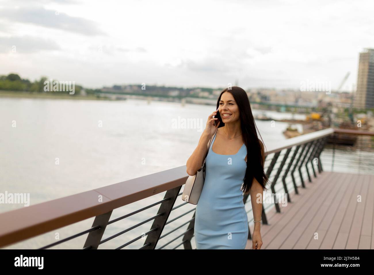 Pretty young woman using a mobile phone while walking on the river ...