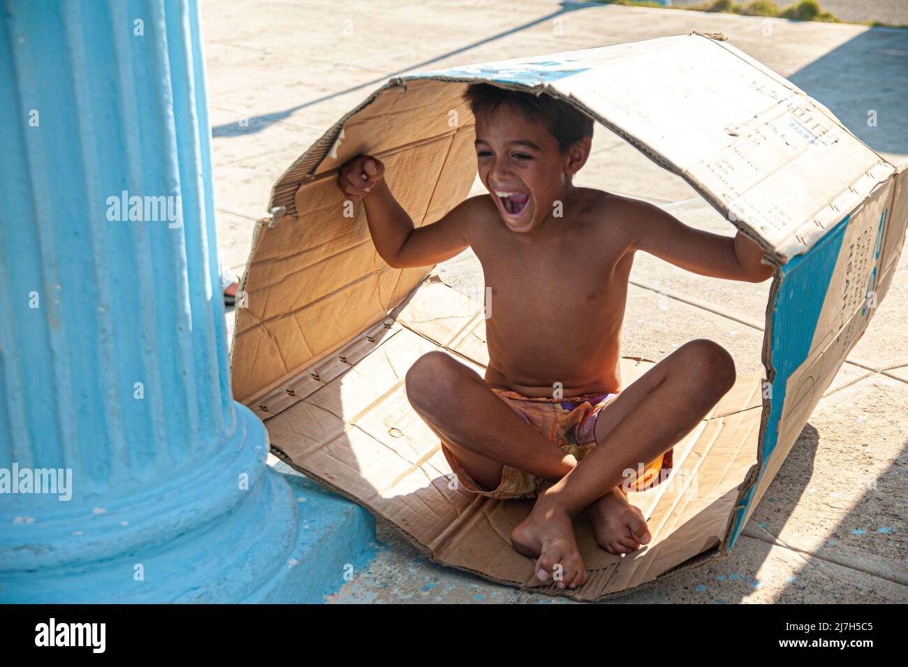 Young barefoot boy laughing while playing in a paper box in Havana, Cuba. Stock Photo