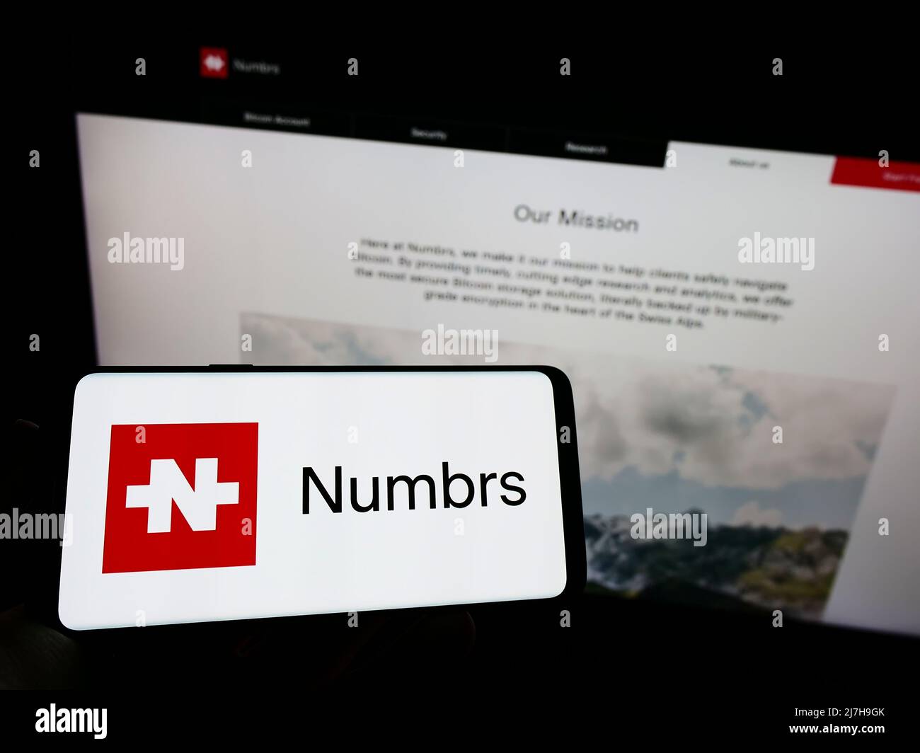 Person holding mobile phone with logo of Swiss fintech company Numbrs Personal Finance AG on screen in front of web page. Focus on phone display. Stock Photo