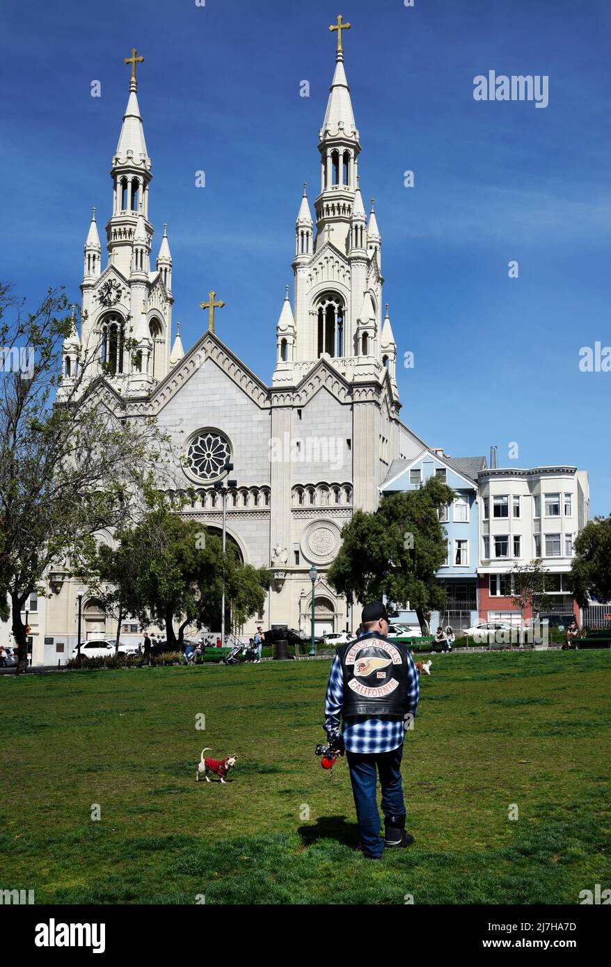 A man wearing a Hell's Angels motorcycle club jacket walks his dog in front of Saints Peter and Paul Catholic Church in San Francisco, California. Stock Photo
