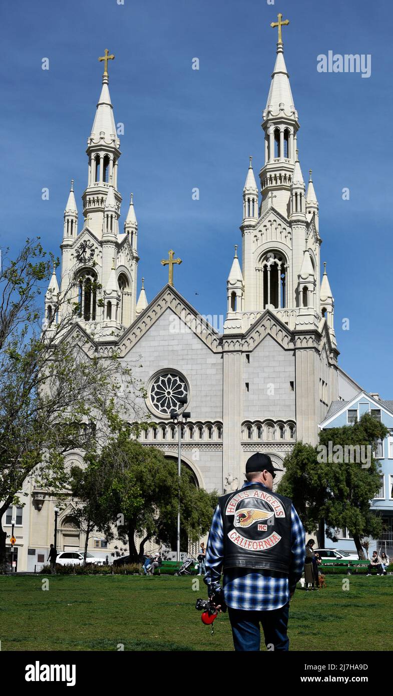 man wearing a Hell's Angels motorcycle club jacket walks his dog in front of Saints Peter and Paul Catholic Church in San Francisco, California. Stock Photo