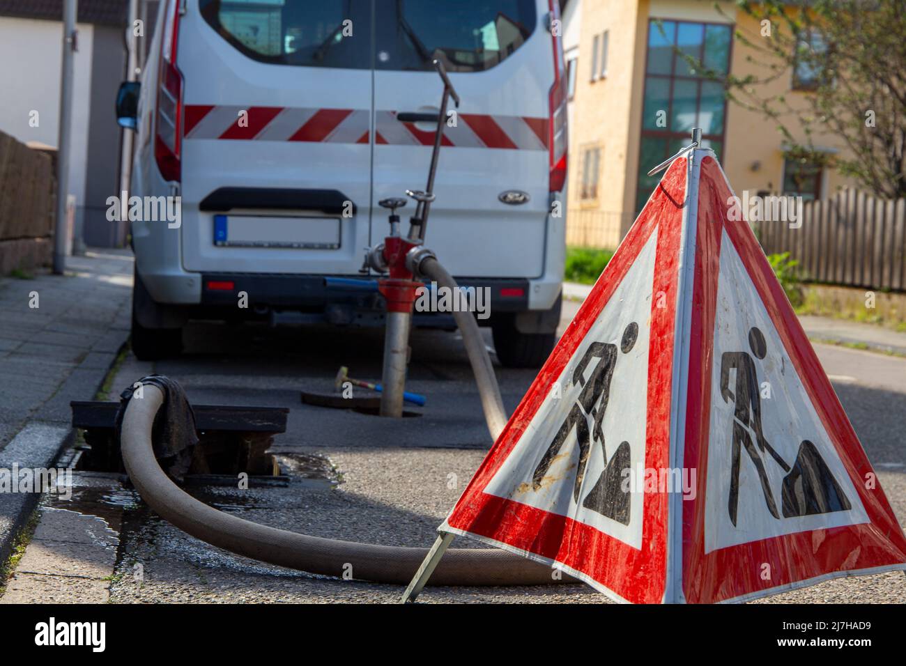 Sewer work: In the foreground a construction site sign, in the background the road drain and the emergency vehicle Stock Photo