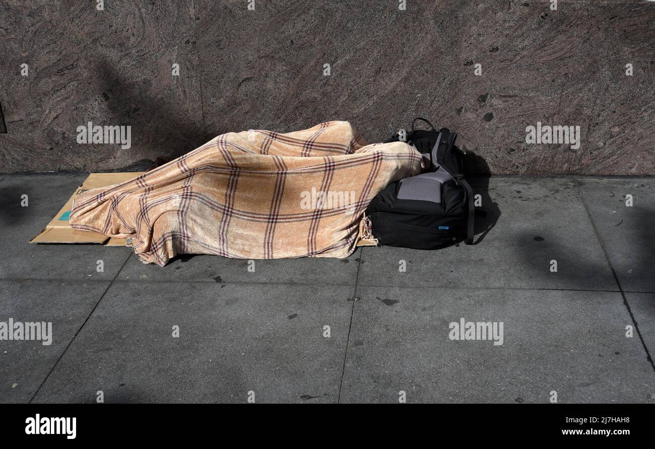 A homeless man sleeps under a blanket on a sidewalk in the North Beach